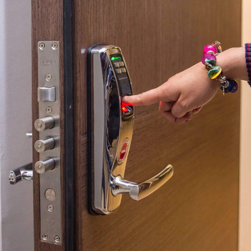 Dedo sobre el lector de huella de una cerradura electrónica en una puerta de madera