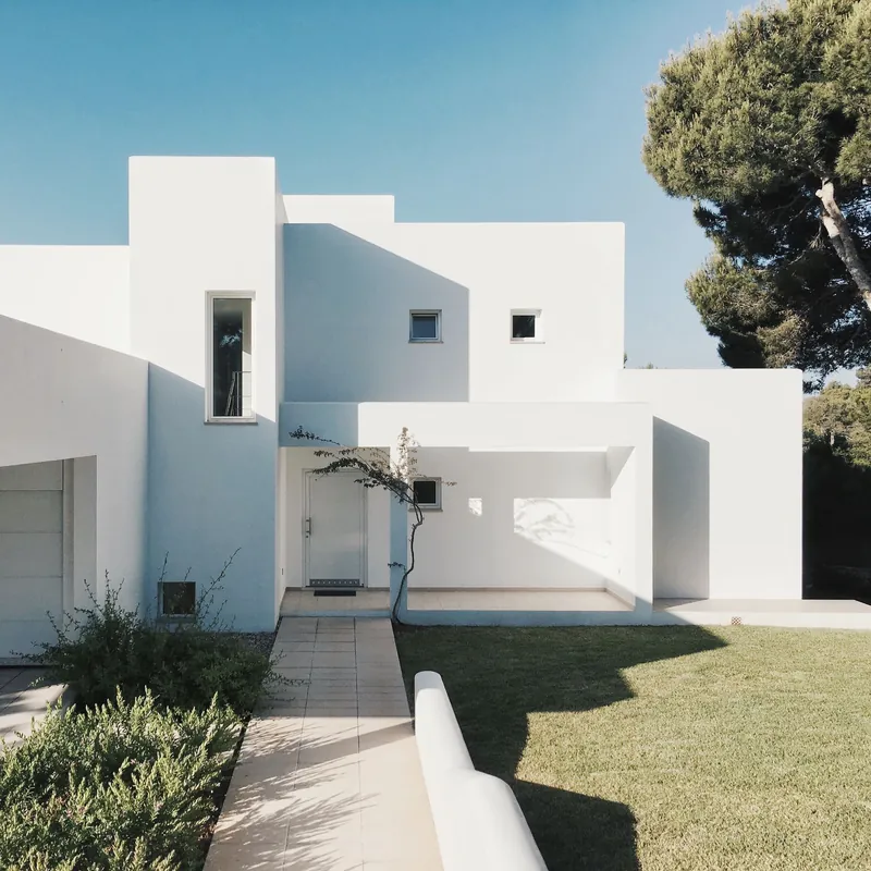 Chalet blanco de estilo mediterráneo con jardín de césped y pinos