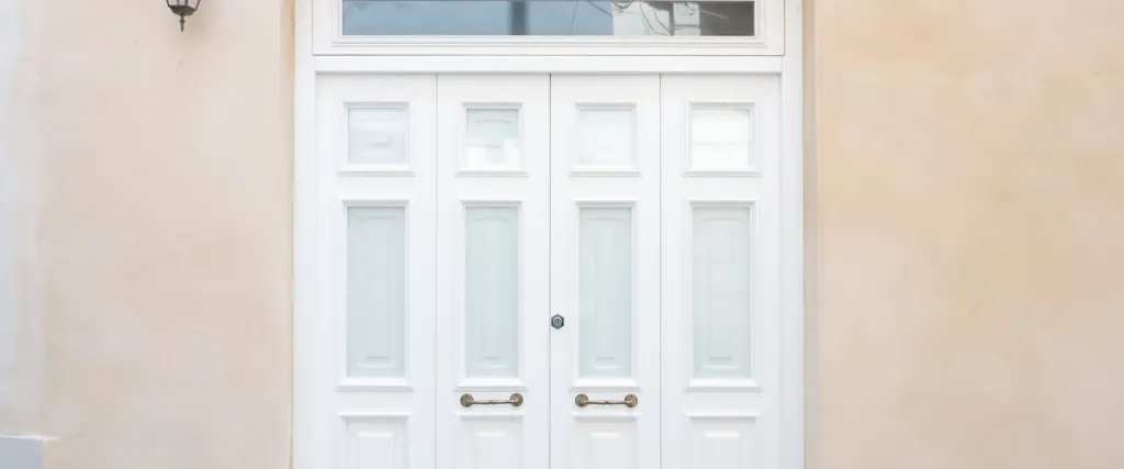 Puerta de entrada blanca de doble hoja en la fachada de una vivienda, a plena luz del día