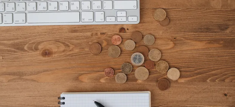 Monedas de euro sobre una mesa de madera junto a un teclado y una libreta