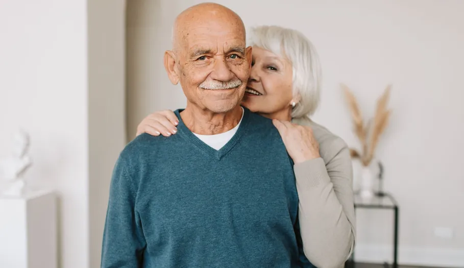 Pareja de mayores sonriente abrazada en el salón de su casa