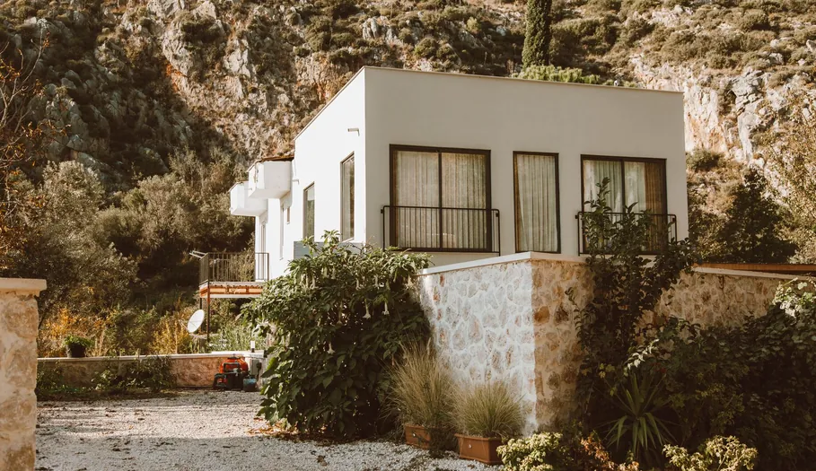 Casa unifamiliar blanca con muro de piedra y jardín al pie de una montaña